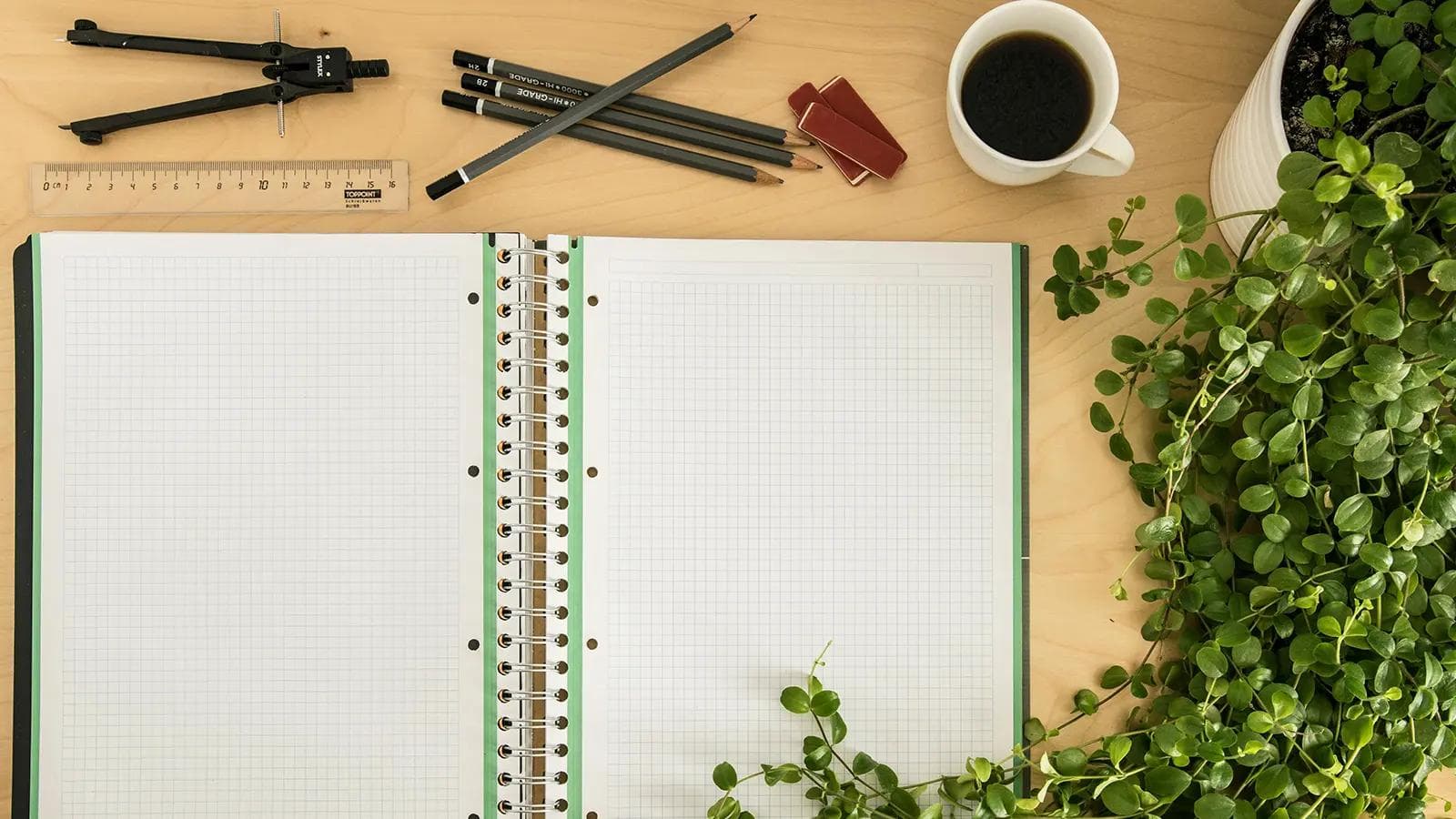 Active Recall vs. Passive Review: Why You're Studying Wrong (And How to Fix It) Overhead view of a study desk with an open blank grid notebook, coffee cup, plant, pencils, compass, and ruler, ready for studying or note-taking.
